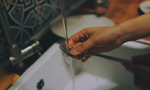 Photograph of a person washing dishes, specifically focusing on a fork. In the image, only a part of their body is visible: the hand.