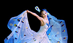 Photograph of a woman dancing in a white dress adorned with blue feathers.