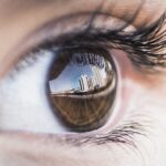 Close-up of a brown eye. In the reflection you can see a balcony screen in the foreground and, in the distance, other buildings, suggesting that the model is on the balcony of an apartment.