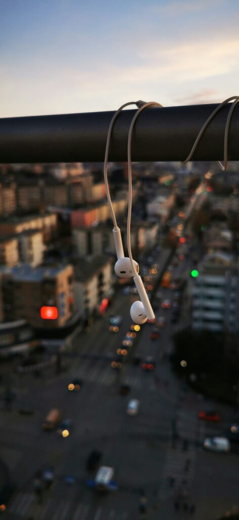 Image focused on white headphones hanging against a twilight sky and a blurred urban background.
