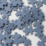 Photograph of gray jigsaw puzzle pieces scattered on a surface.