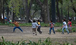 Foto de seis niños jugando con una pelota en una plaza. Es un espacio con muchos árboles y plantas.