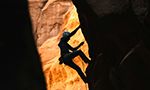 Fotografía de una persona escalando un cañón. La persona está en medio del recorrido, dirigiéndose a la cima.