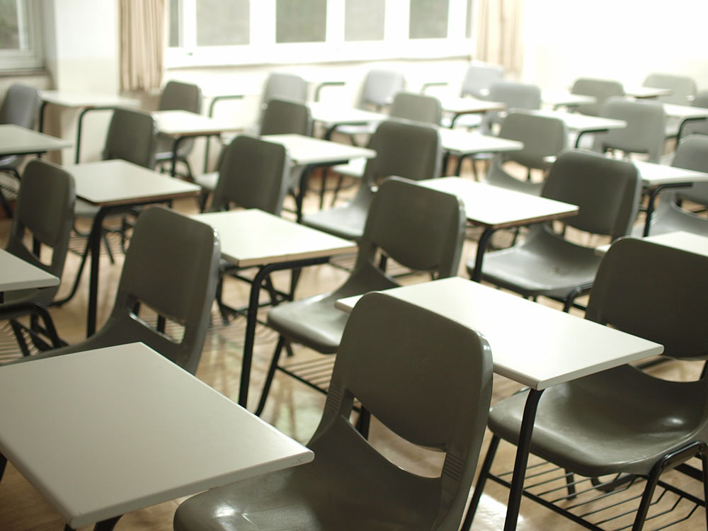 Foto: uma sala de aula com várias cadeiras vazias.