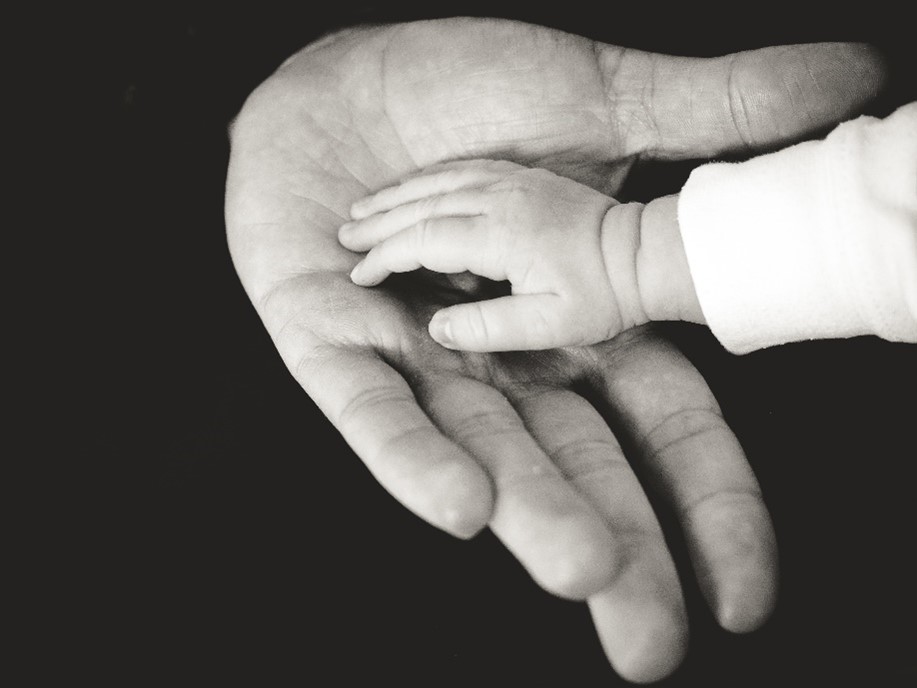Mão aberta de um adulto tocando a mão de uma criança, foto em preto e branco.