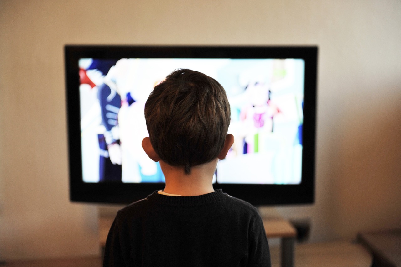 Imagem de uma criança de costas assistindo televisão