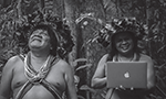Print de uma foto no Instagram. O nome do perfil é "midiaindiaoficial". Na foto, duas pessoas indígenas estão sorrindo. no fundo, parte de uma floresta. Uma das pessoas está segurando um notebook. Na legenda, "Conectados com a floresta - via Ubiratan Surui". Publicada em 26 de novembro de 2019.