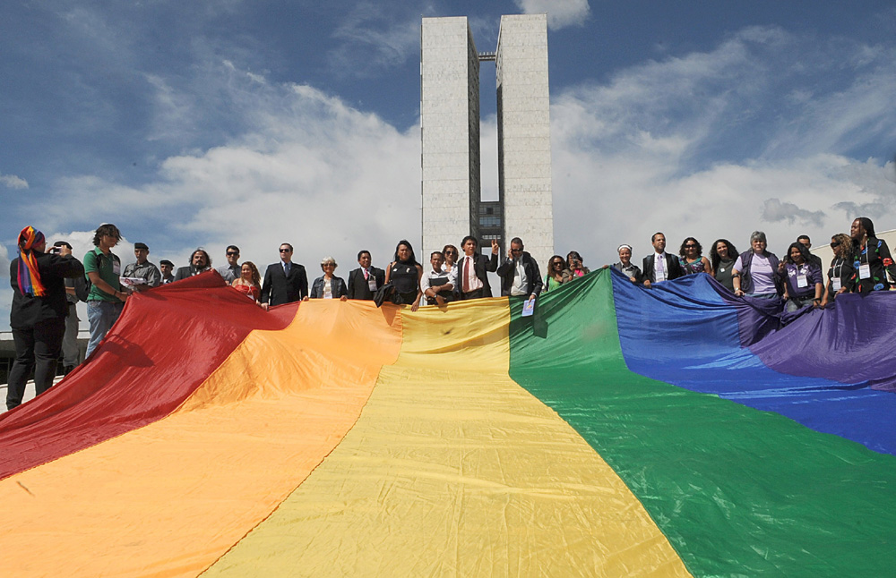 Grupo de pessoas segurando a bandeira LGBT em frente ao Congresso Nacional.