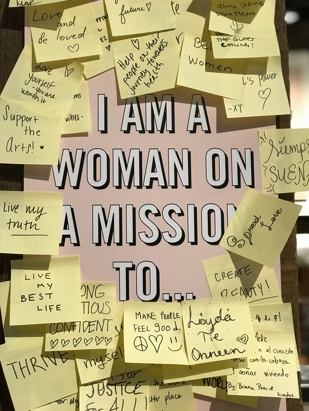 Poster de fundo rosa com a frase em inglês "I am a woman on a mission to..." e cercado por vários post-its contendo mensagens de positividade.