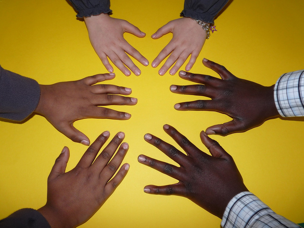 Círculo de mãos abertas de cinco crianças, incluindo duas de pele negra e uma de pele branca, sobre um fundo amarelo.