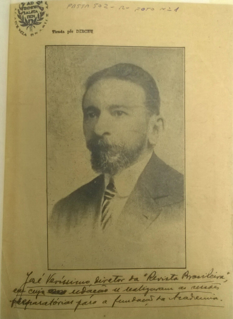 Fotografia de época, em preto e branco, de José Veríssimo, um homem com barba, usando terno, com texto manuscrito na parte inferior.