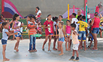 Fotografia mostrando várias crianças brincando no pátio de uma escola, com pais e mães observando das arquibancadas ao fundo.