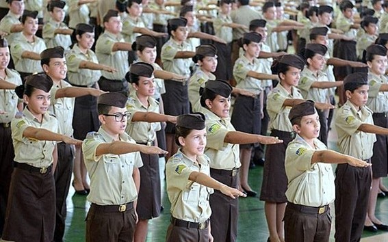 Fotografia de crianças com uniformes de escola militar e com um dos braços esticados para frente Fotografia de crianças com uniformes de escola militar e com um dos braços esticados para frente