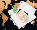 Fotografia de um mapa mundi preto e amarelo aberto com folhas, caneta e um caderno em cima dele